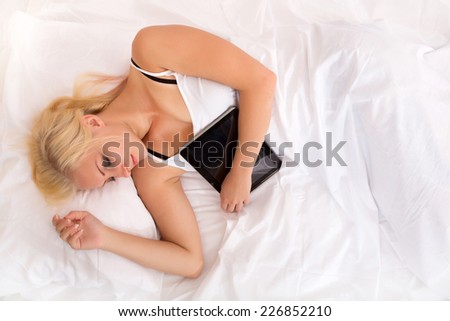 Portrait of a blonde girl sleeping in a bed holding a tablet pc.