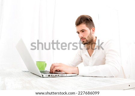 Attractive young man sitting at the table with a laptop computer.