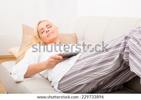 A mature woman in pyjamas sleeping with a tablet PC on the sofa.