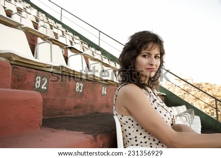 A vintage style dressed girl sitting in a sports stadium alone.