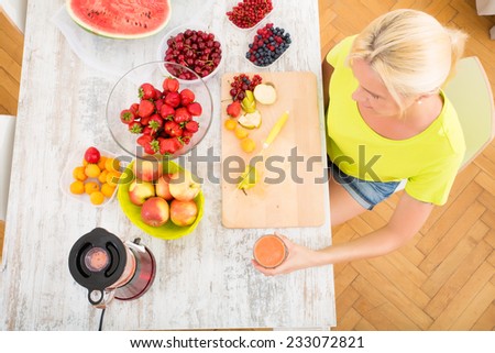 A beautiful mature woman enjoying a smoothie or juice with fruits in the kitchen.