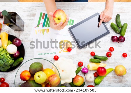 Close-up of a young adult woman informing herself with a tablet PC about nutritional values of fruits and vegetables.