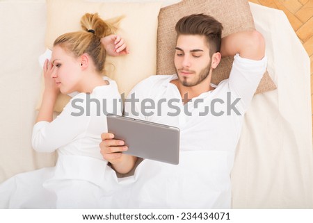 A young and happy couple with a tablet PC  in bed from above.