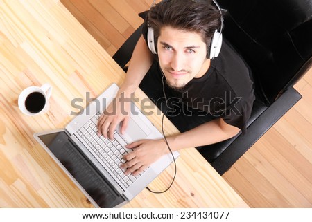 A young hispanic man working on a laptop computer while listening to music with headphones.