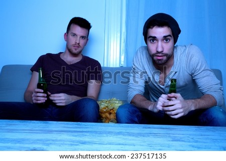 Two Friends watching passionately TV with Beer and Potato Chips.