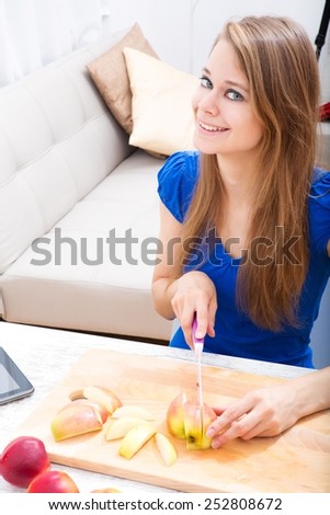 Young woman preparing fruit juice while getting online information about nutrition.