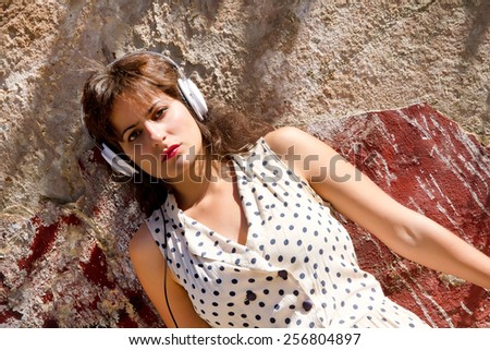 A vintage dressed girl listing to music in a urban environment.