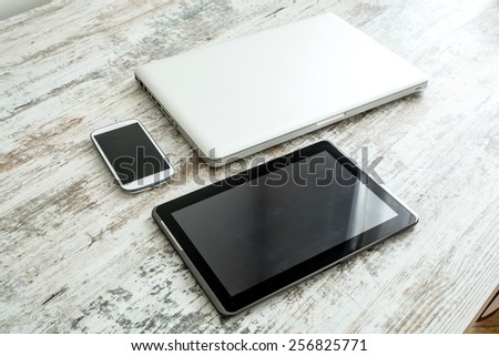 A smartphone, a tablet computer and a laptop computer on a wooden desktop.