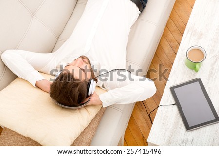 A young man relaxing and listening to music on the couch.