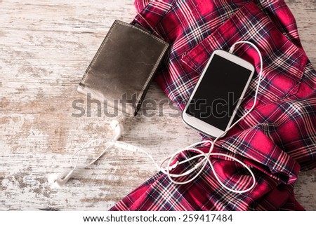 Red pants, a wallet and a smartphone with plugged in earphones on the table.