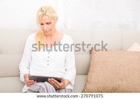 A mature woman in Pyjamas with a Tablet PC on the Sofa.