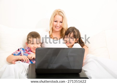 A mother using with her son and daughter a laptop computer in bed.