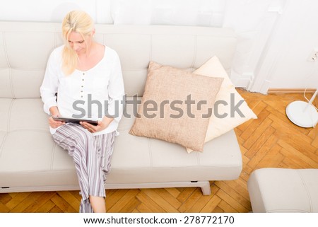 A mature woman in pyjamas with a tablet PC on the sofa.
