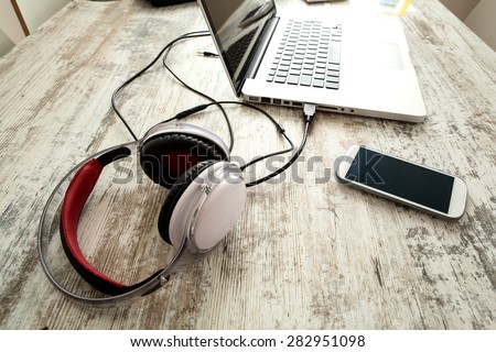 Smartphone, Headphones and Laptop on a wooden Desktop.