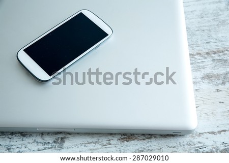 A Smartphone and a switched off laptop computer on a wooden Desktop.