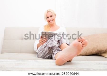 A mature woman in Pyjamas with a Tablet PC on the Sofa. Focus on the Toes.