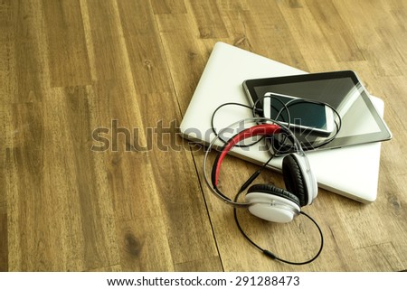 A Laptop computer, Headphones, a Tablet PC and a Smartphone on a wooden Desktop.