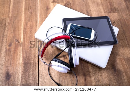 A Laptop computer, Headphones, a Tablet PC and a Smartphone on a wooden Desktop.
