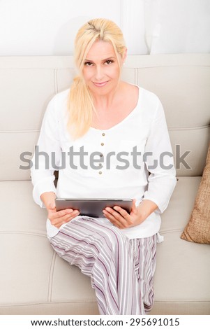 A mature woman in pyjamas with a tablet PC on the sofa.