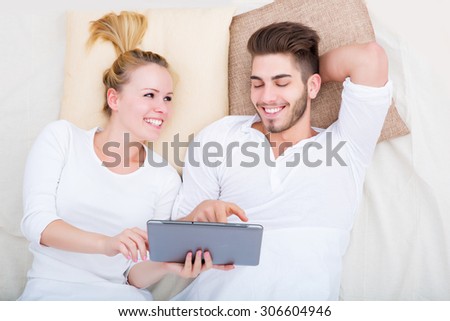 A young and happy couple with a tablet PC  in bed from above.