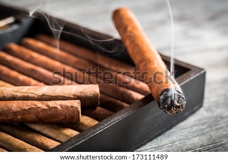 Burning Cigar With Smoke On Old Humidor