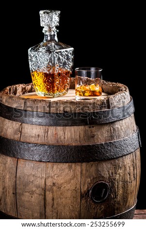 Glass of golden aged brandy or whiskey and old oak barrel