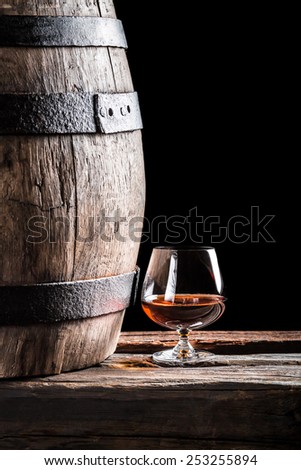 Glass of cognac and old oak barrel