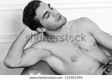 handsome young male model posing on sofa. Black-and-white photo.