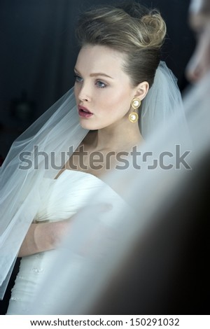 beautiful bride brunette girl in white wedding dress with hairstyle and bright makeup looks in the mirror