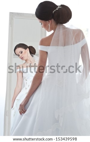 beautiful bride brunette girl in white wedding dress with hairstyle and bright makeup looks in the mirror
