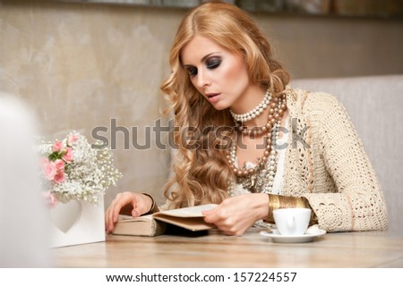 Beautiful young woman sitting in a cafe drinking coffee and reading a book