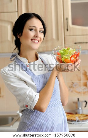 Smiling woman cook holds a bowl of salad on the kitchen