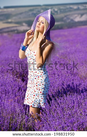 Beautiful girl in violet hat on the lavender field. Young woman with long hair collects lavender