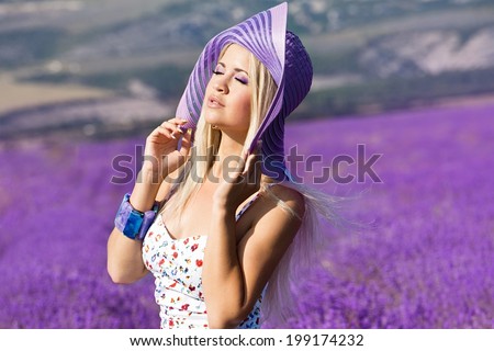 Beautiful girl in violet hat on the lavender field. Young woman with long hair collects lavender
