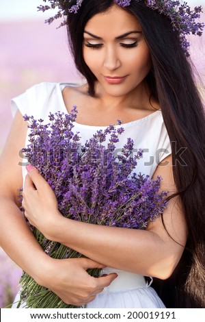 Beautiful girl with long dark hair in lavender wreath on the lavender field. Young woman with long hair collects lavender