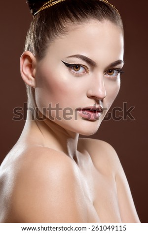 Beauty portrait of attractive model face with bright visage. Gold eye makeup and soft beige lips make-up. Gold arrow make up