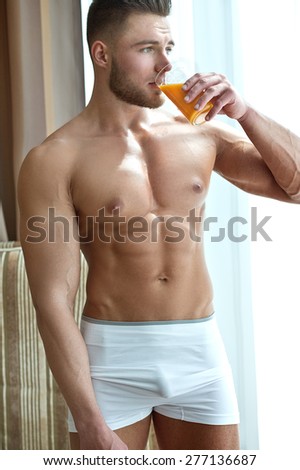 Beautiful muscular male model near window with orange juice