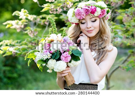 Bride. Beautiful young blond woman in the park with flower wreath and bouquet on a warm summer day.