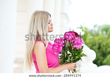 Beautiful woman with long beautiful hair in a pink dress posing with a bouquet of peonies