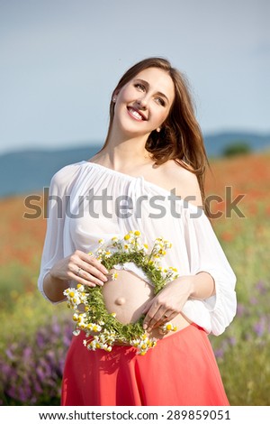 Happy pregnant woman with flower wreath in meadow flowers, sunset time, new life concept