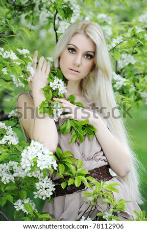 Young beautiful blonde woman in a dress in blooming apple garden