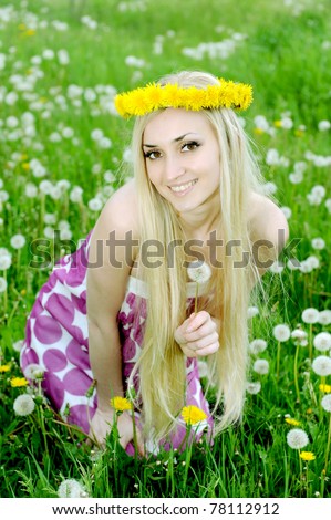 Young pretty woman in wreath of dandelions sits in the meadow at solar day
