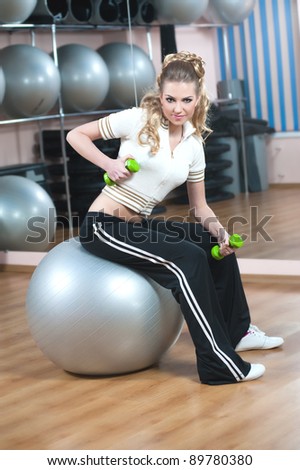 Portrait of fitness woman working out with free weights in gym on fitness ball