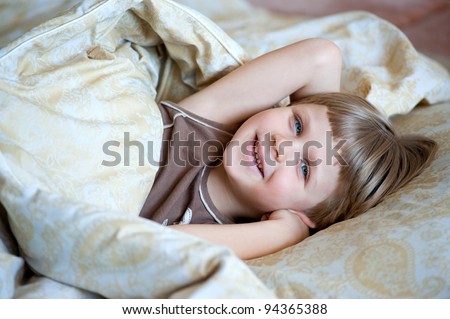 Little smiling boy in bed under the blanket
