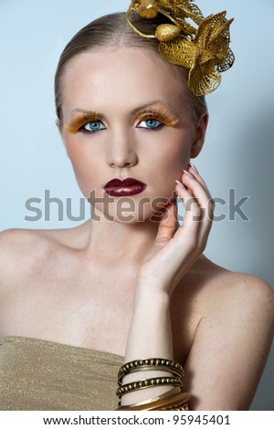 woman with gold make up and gold earrings and bracelet visible near her face