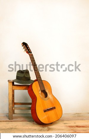 Spanish guitar with hat leaning on a stool in front of a white wall