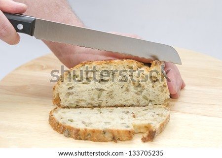 Human hands with a knife cutting a loaf of bread on the wooden board