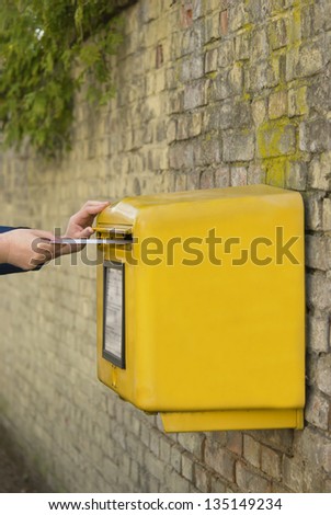 Man\'s hands posting a letter in a yellow post box, stone wall background