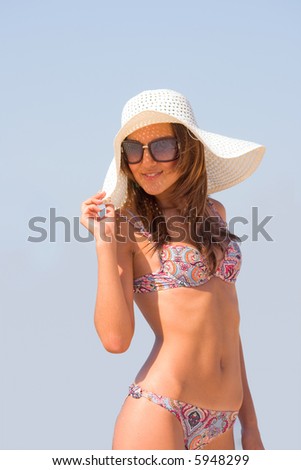 Young beautiful sexy tanned brunette woman with hat and bikini laying on sea beach