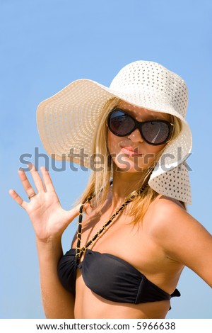Young beautiful sexy tanned blond woman with hat and bikini laying on sea beach